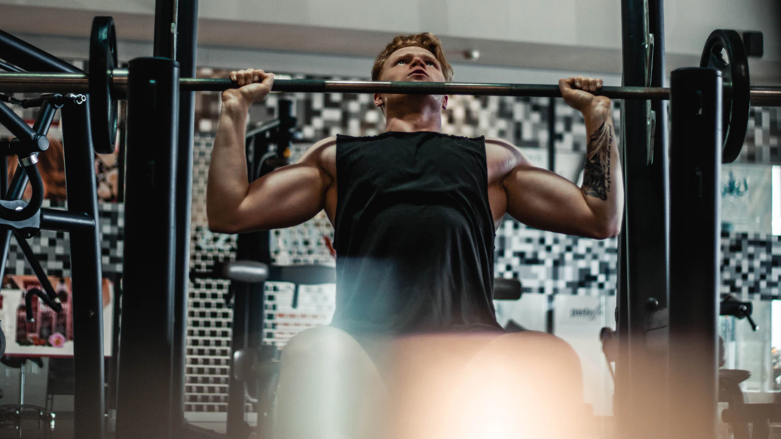 A man pressing a barbell overhead in a gym