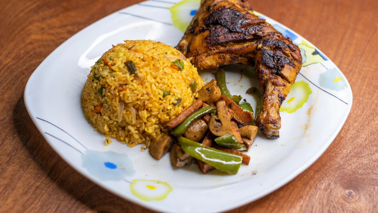 A plate of grilled chicken leg with fried rice and stir-fried vegetables