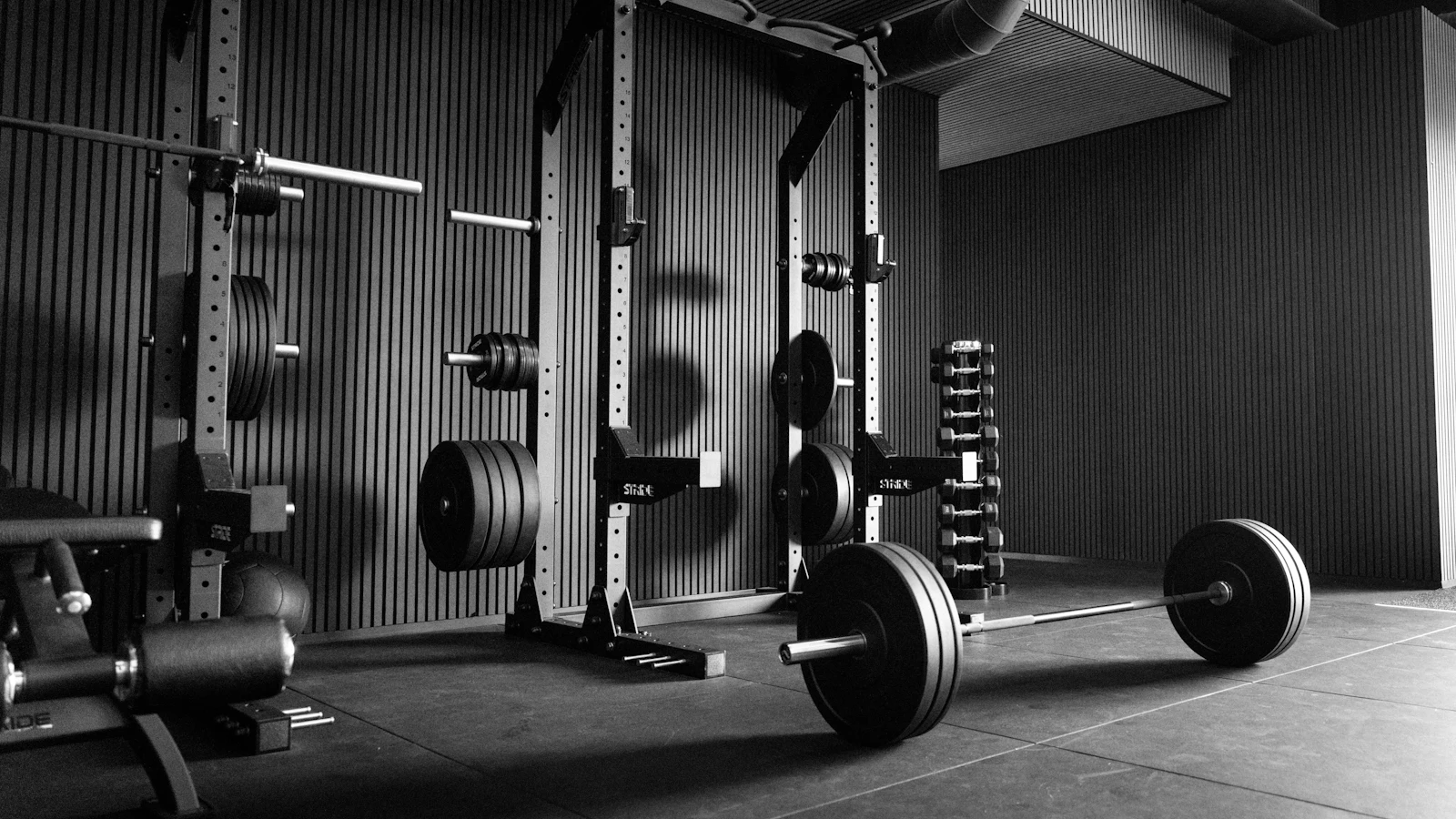 An empty gym with power racks, a loaded barbell and dumbbells