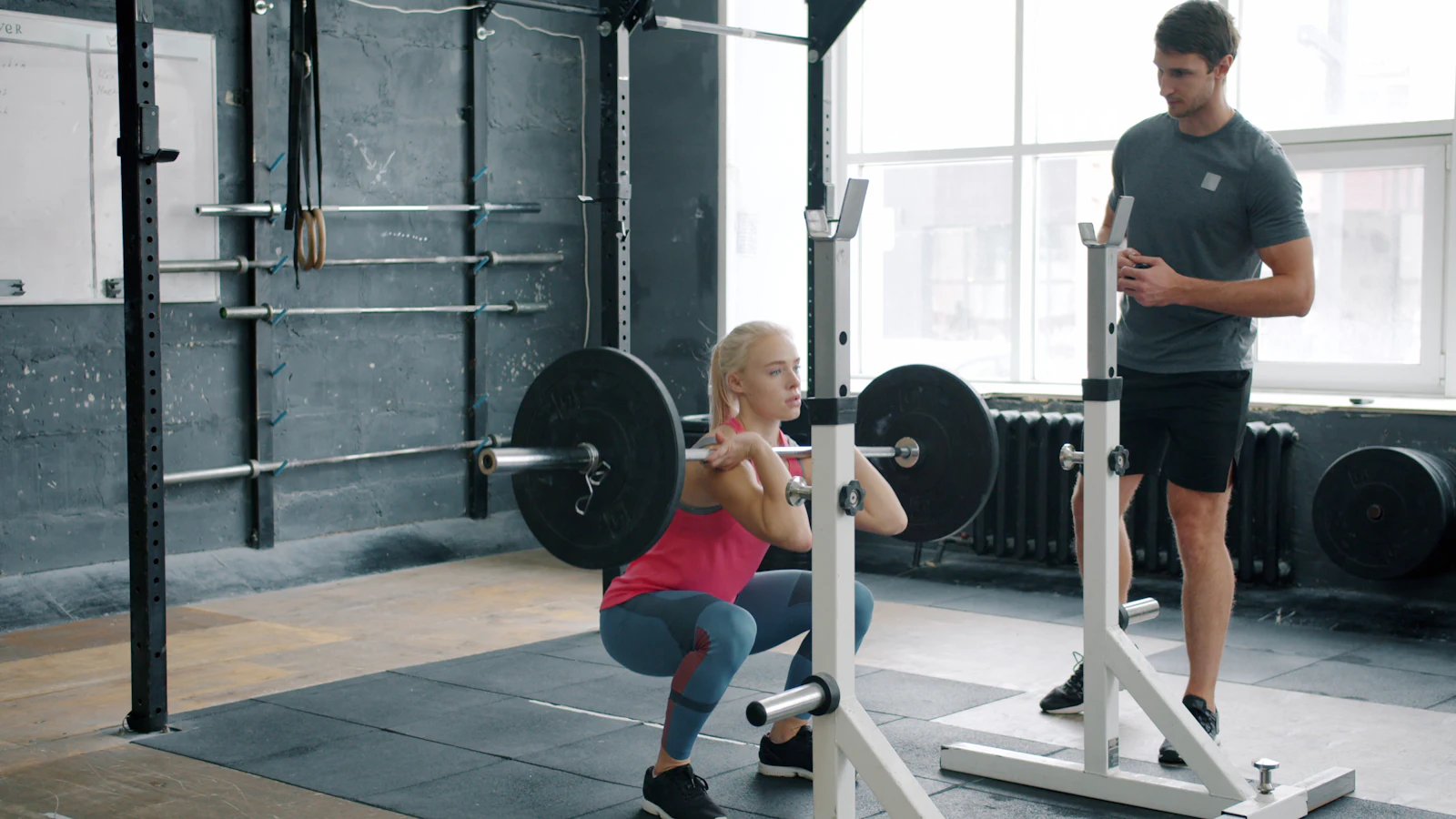 A woman performing a barbell front squat in a rack while a trainer watches